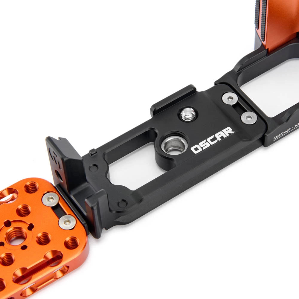 A close-up of a black metal camera mounting bracket with the brand name OSCAR printed in white, connected to an orange anodized aluminum quick-release plate on a white background.