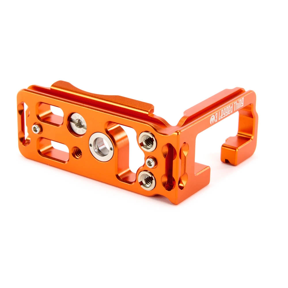 An orange anodized aluminum mounting bracket with silver screws, shown on a clean white background. The brand name '3 Legged Thing' is printed in white on the right side.