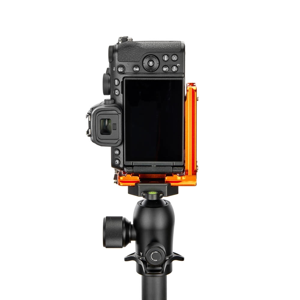 An orange protective camera housing mount holding a black Mirrorless camera, mounted on a black tripod, shown against a solid white background.