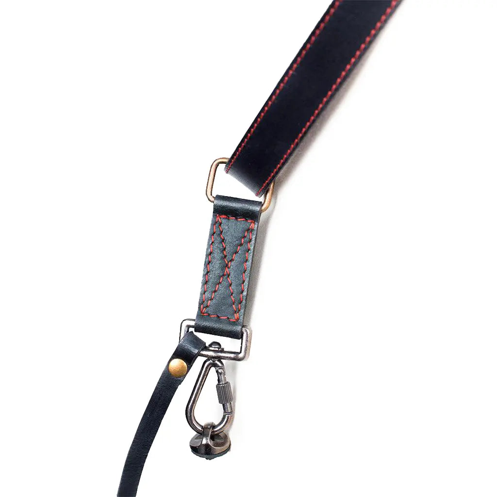 Close-up of a black leather strap with red stitching and metal hardware on a white background
