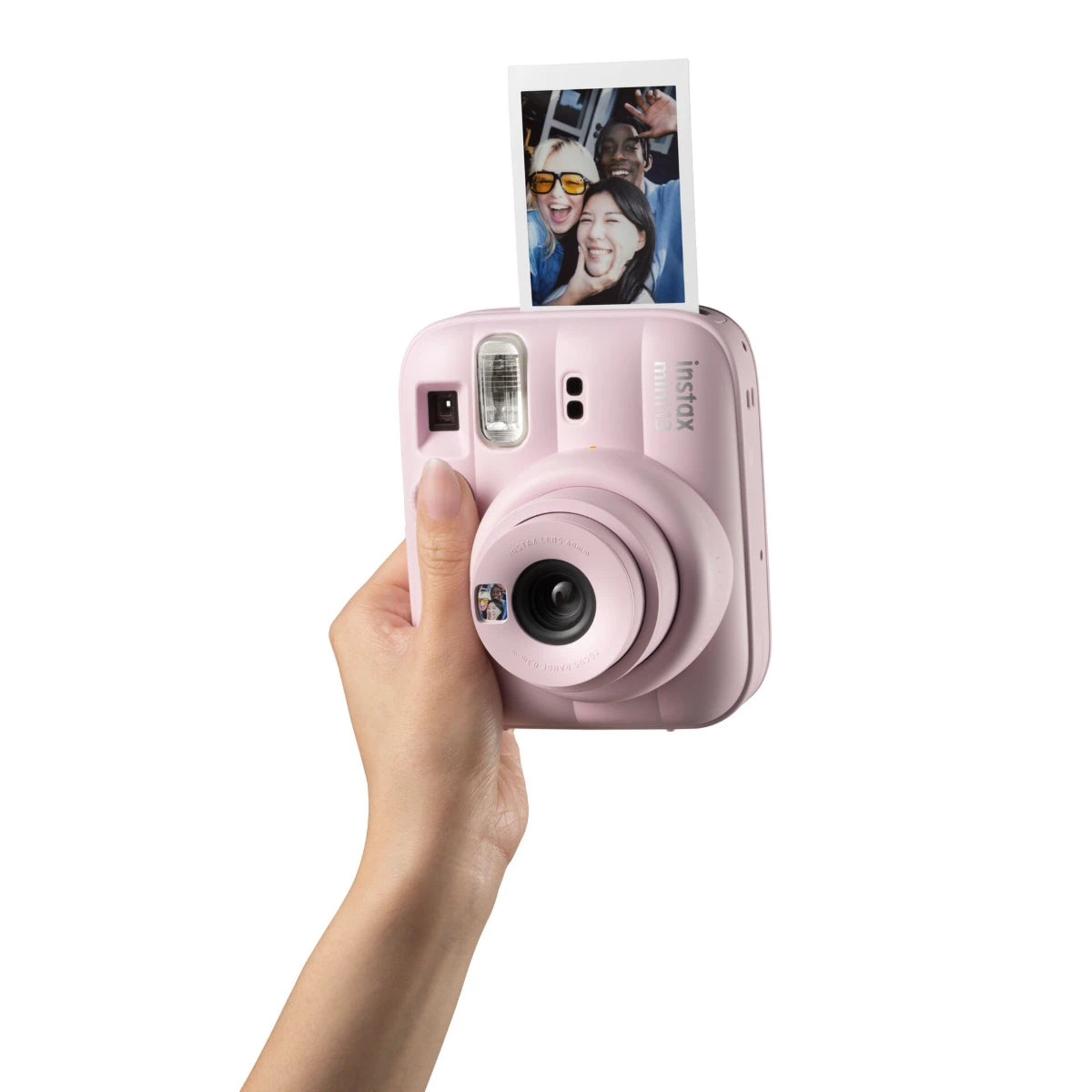 Pink instant camera held by a hand with a photo of people on the top, on a white background