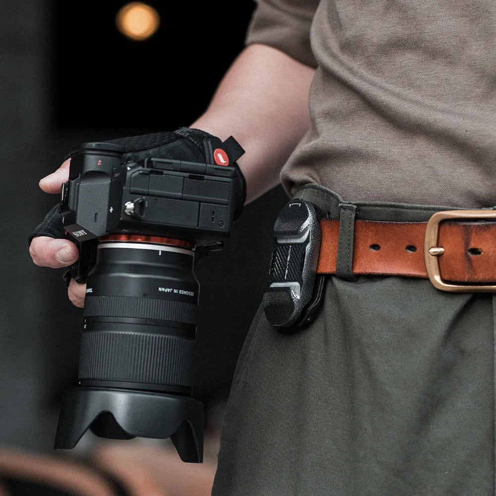 Person holding a camera with a lens, wearing a brown belt.