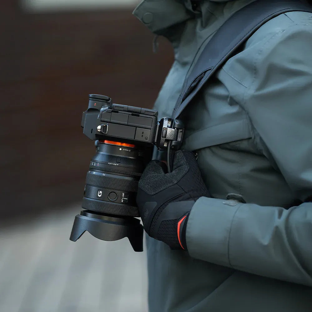 Person holding a camera with a lens attached, wearing a green jacket and black gloves.