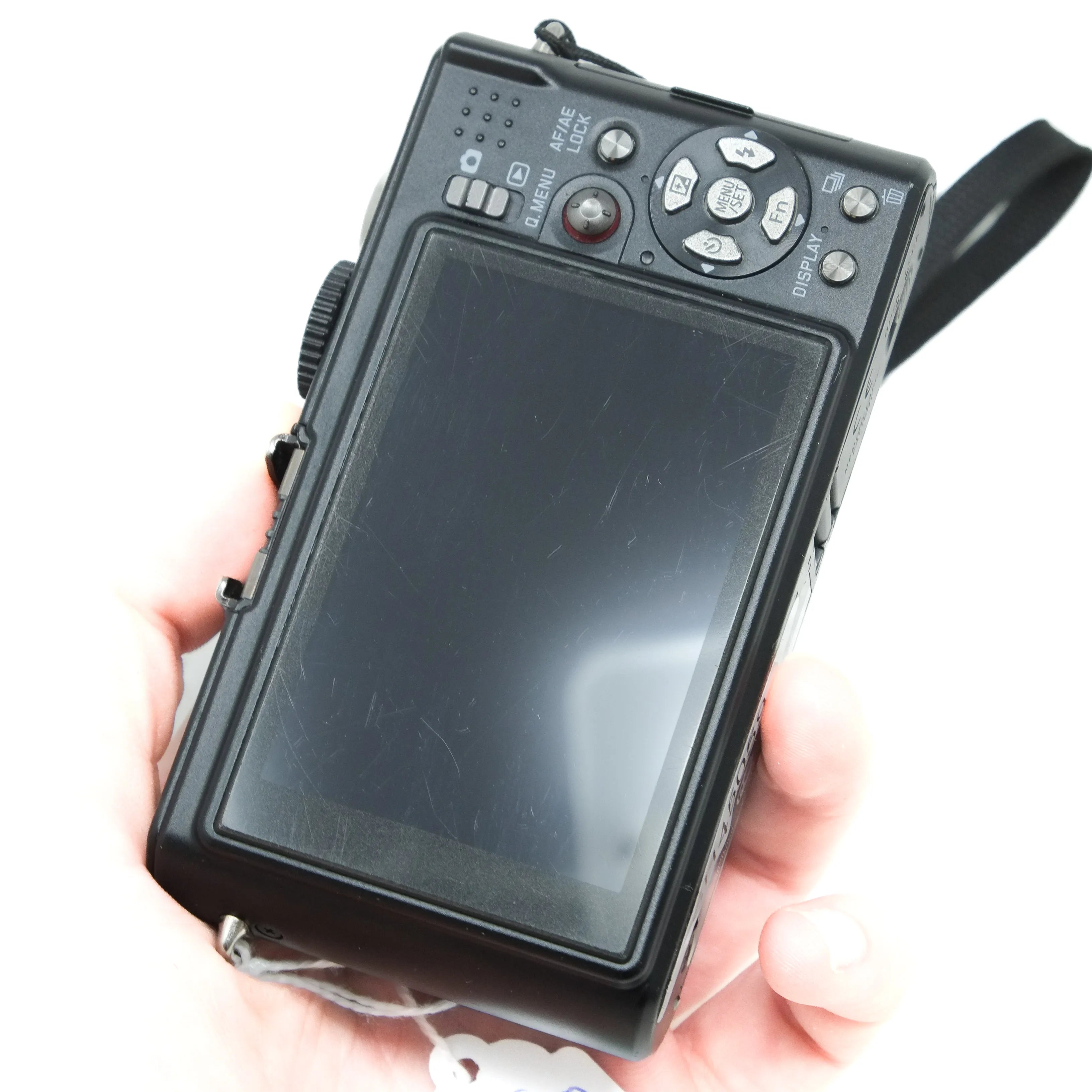 Hand holding a black digital camera with a strap on a white background