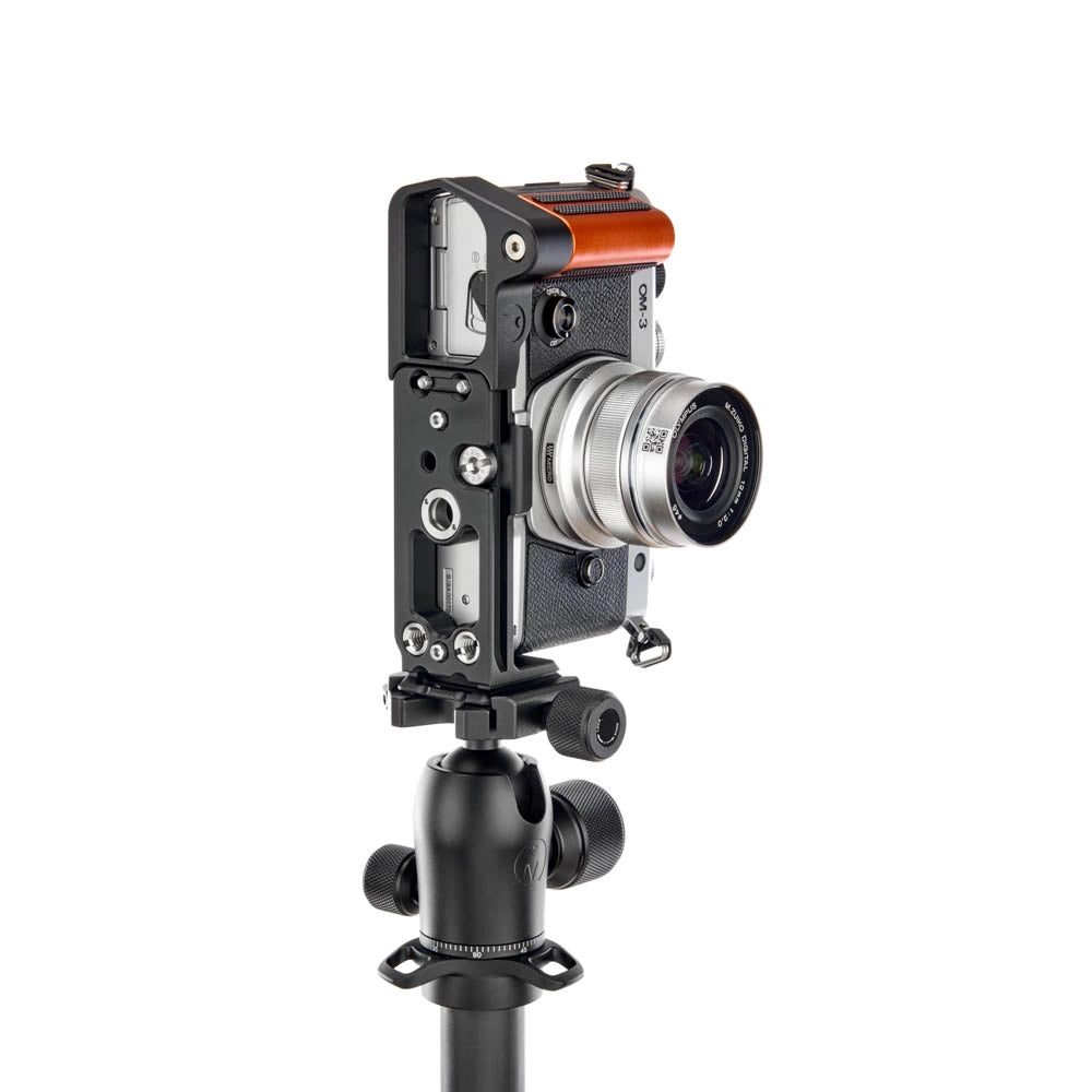 A camera rig with a silver and black camera body, an orange accent on top, and a mounted lens, attached to a black ball head tripod against a solid white background.