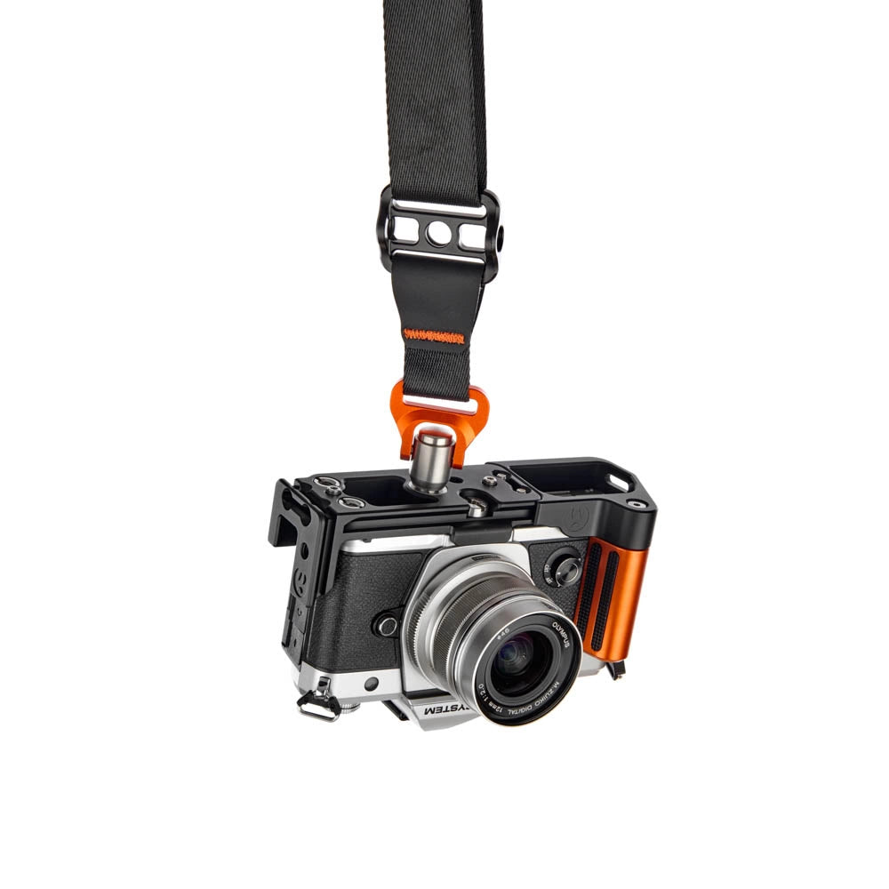 A black camera strap with an orange quick-release clip holding a black and silver OM System mirrorless camera, shown against a plain white background.