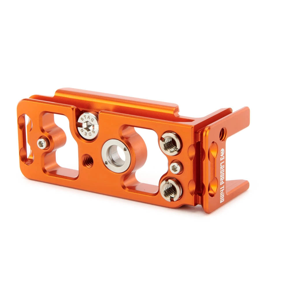 An orange anodized aluminum mechanical component with silver screws and a silver circular center insert, photographed on a clean white background.