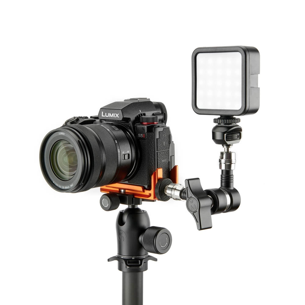 A black Lumix camera with a lens attached, mounted on an orange and black camera rig with a black adjustable arm and a square LED light panel, set against a plain white background.