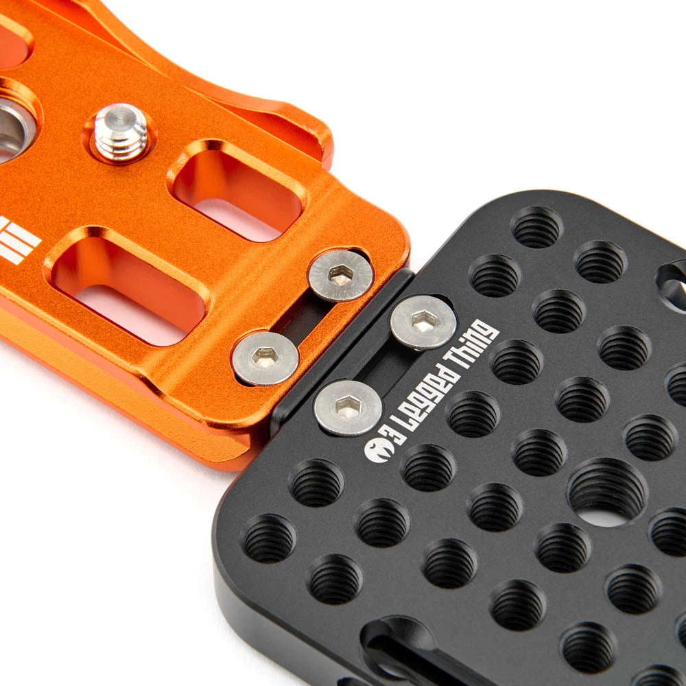 Close-up of a black metal mounting plate with threaded holes and white '3 Legged Thing' branding, attached to an orange anodized aluminum component on a white background.