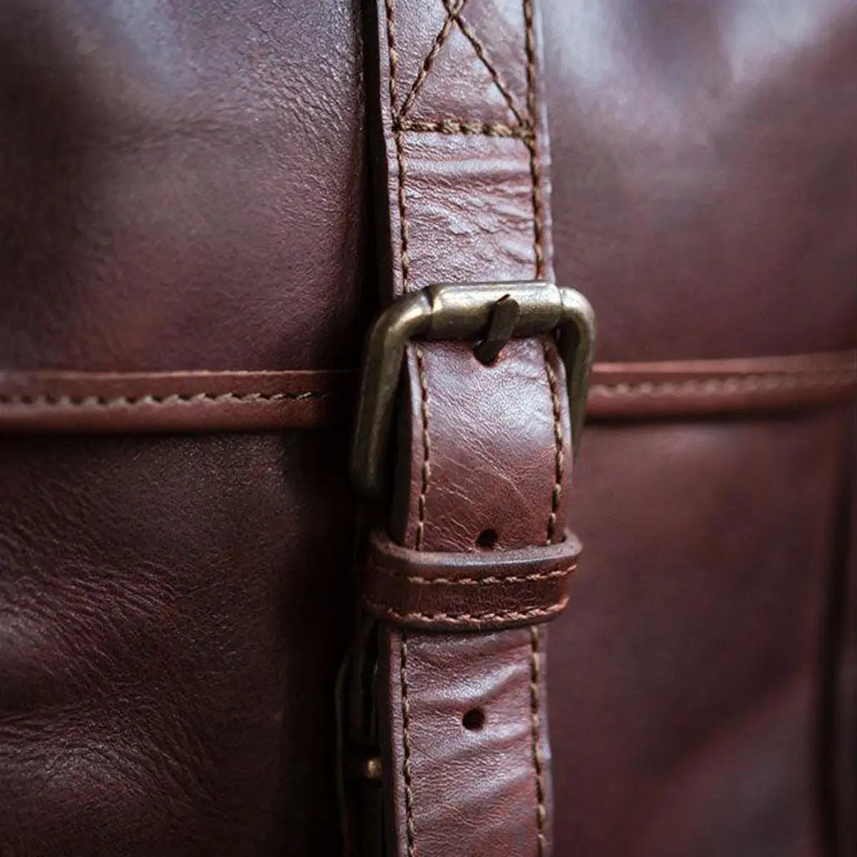 Close-up of a brown leather bag with a brass buckle.