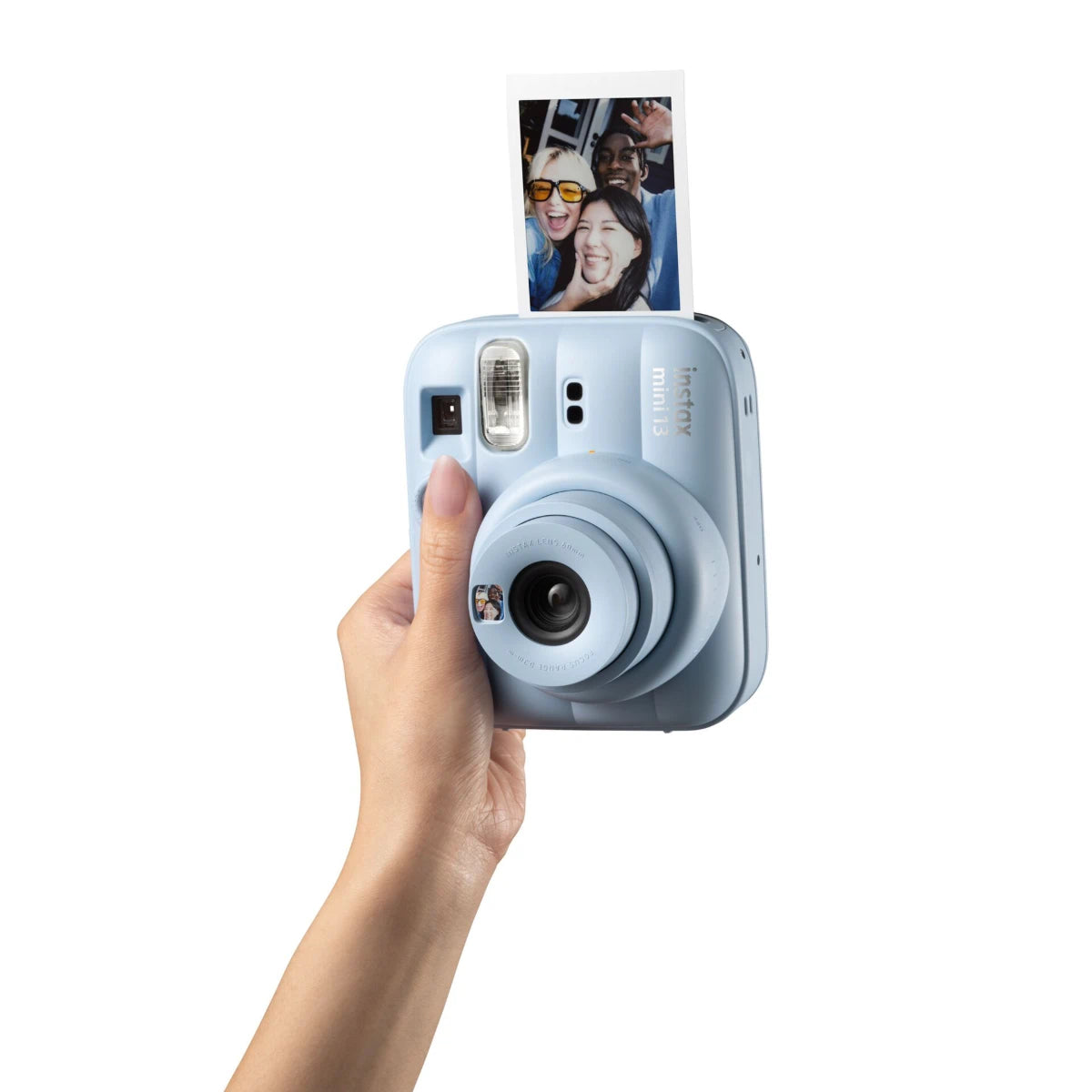 Hand holding a light blue instant camera with a printed photo on a white background