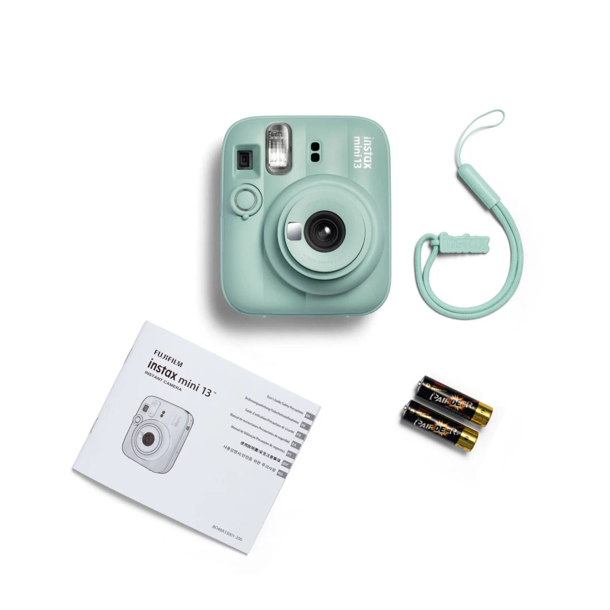 Mint green instant camera with strap, batteries, and instruction manual on a white background