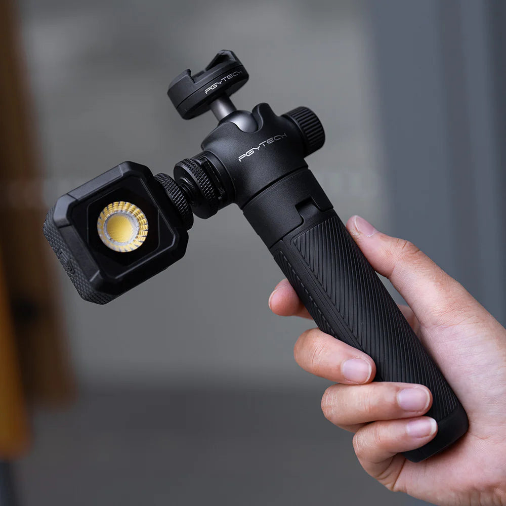 Hand holding a black light stand with a camera mount against a blurred background