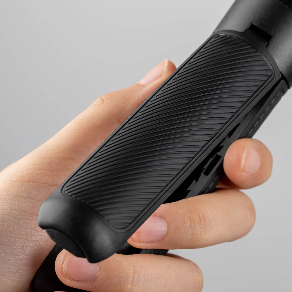 Hand holding a black electronic device with textured grip on a gray background