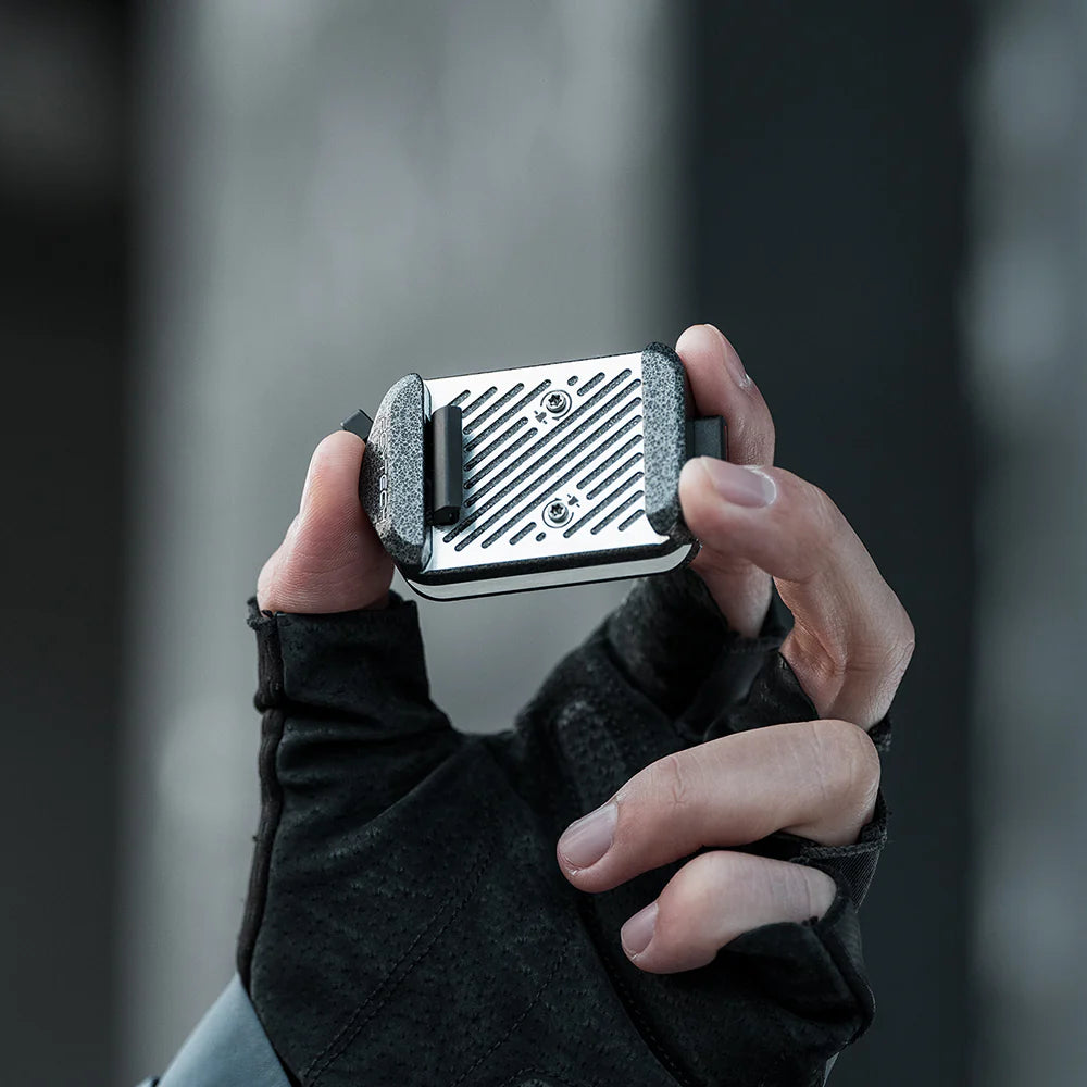 Hand holding a small metallic device with a textured surface against a blurred background