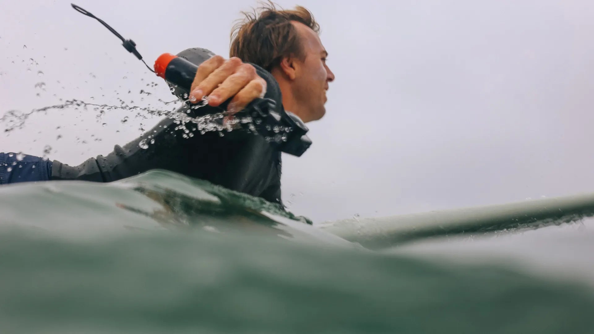 Lifestyle photo of a surder in the waves paddling out out whilst holding the gopro grip